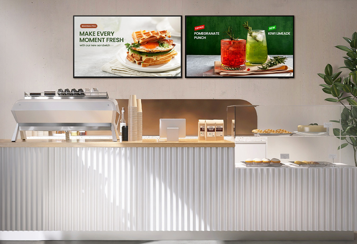 Απεικονίζονται 2 οθόνες πάνω από ταμείο καταστήματος.